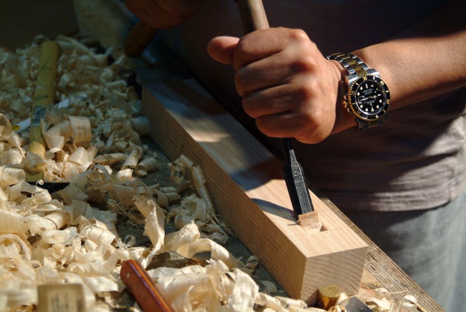 A skilled woodworker carving wood with a sharp chisel tool in a workshop setting.